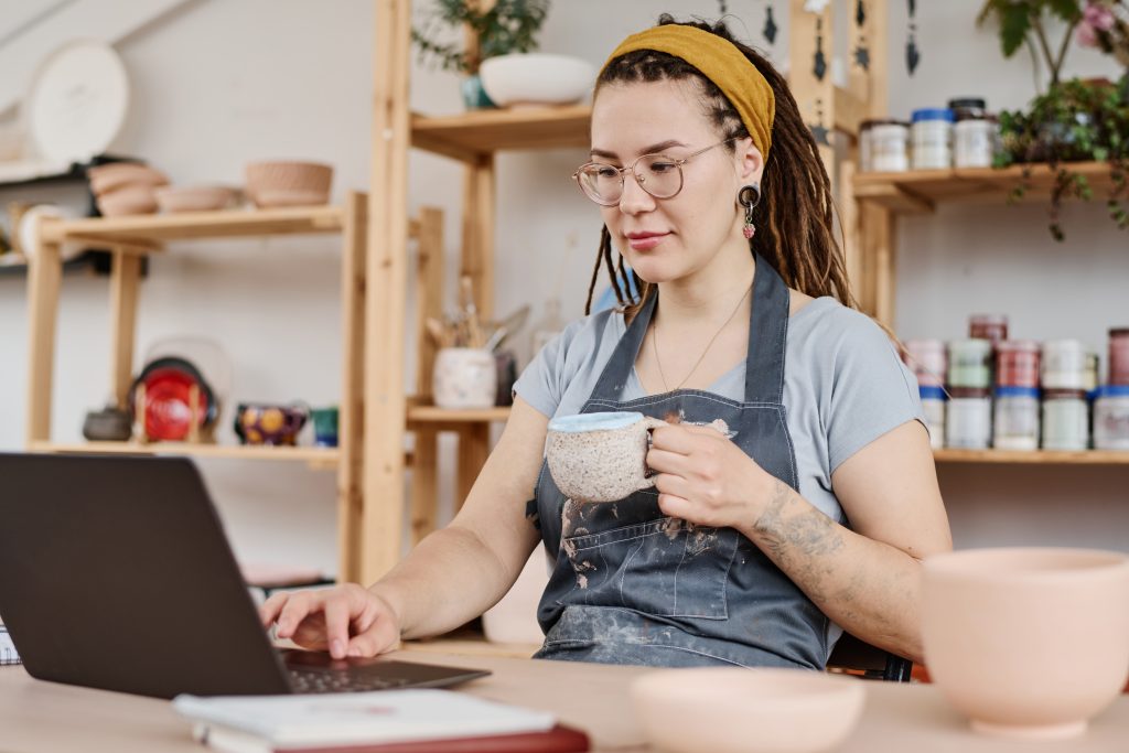 Young female freelancer sitting in front of a laptop, having tea and working on a video tutorial